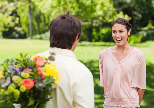 Woman excited as she approaches her friend who has flowers hidden behind his back